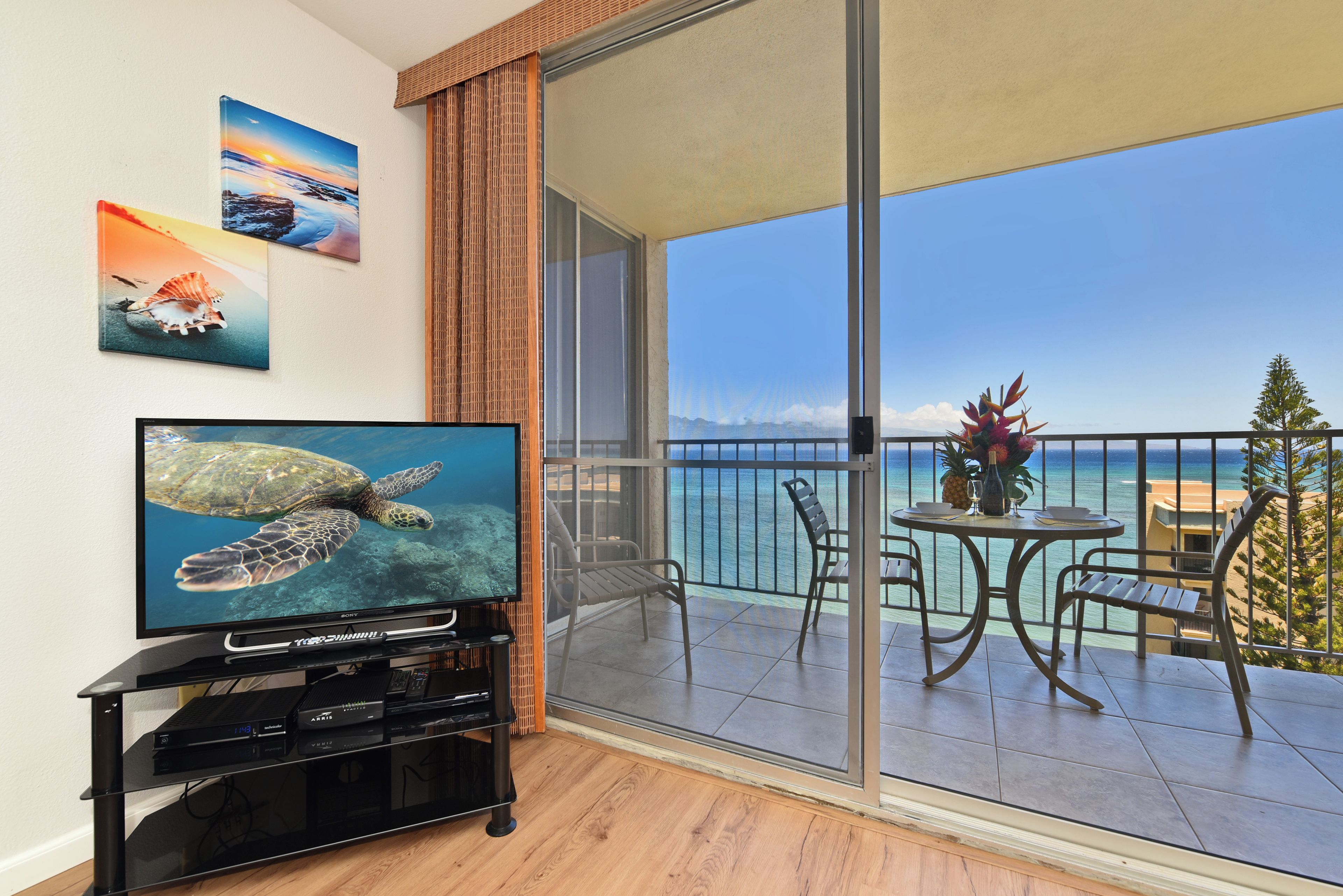 Een balkon met een televisie, eettafel, stoelen en uitzicht op de oceaan.