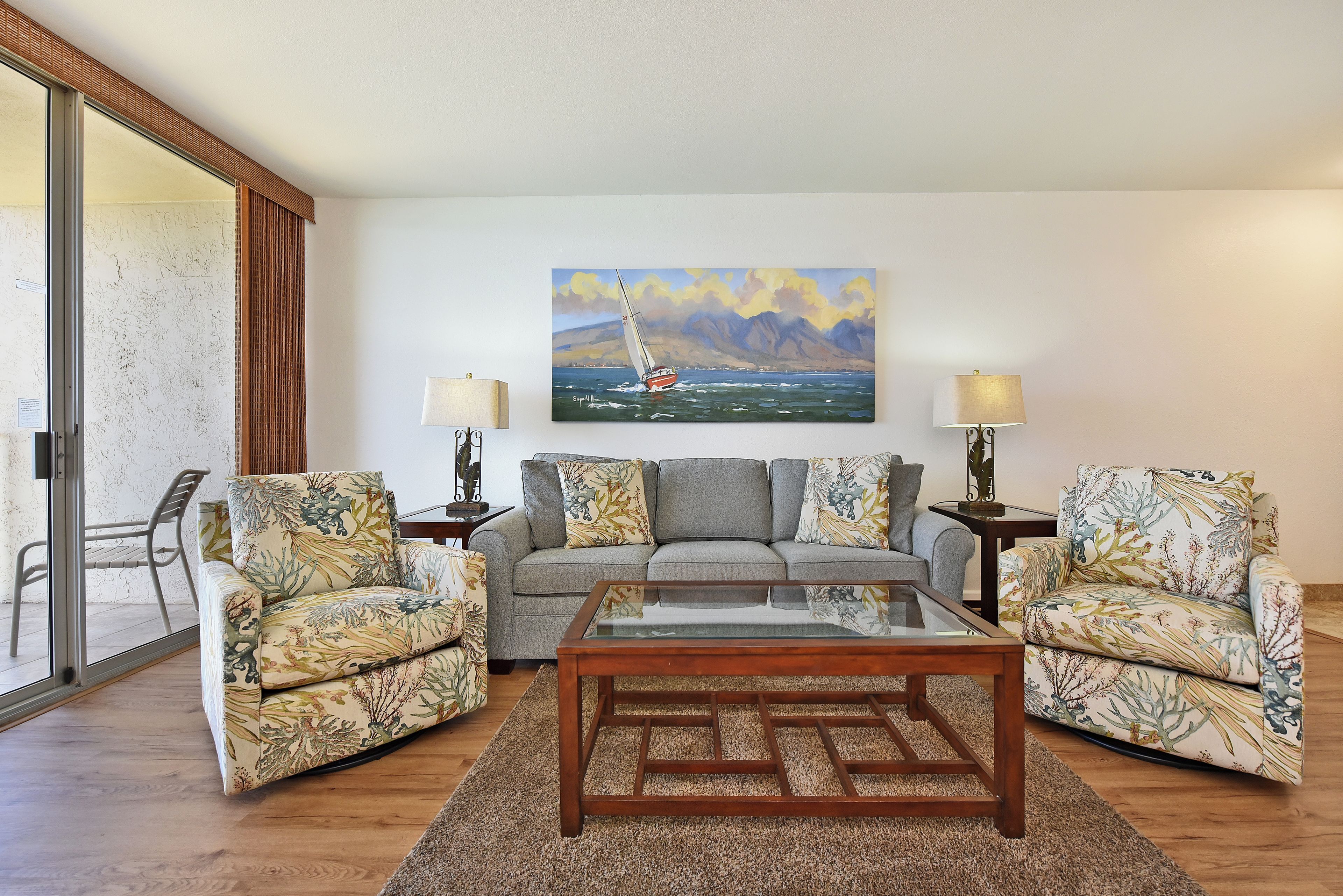 A living room with a sofa, two armchairs, a coffee table, and a painting of a sailboat on the wall.