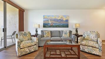 A living room with a sofa, two armchairs, a coffee table, and a painting of a sailboat on the wall.