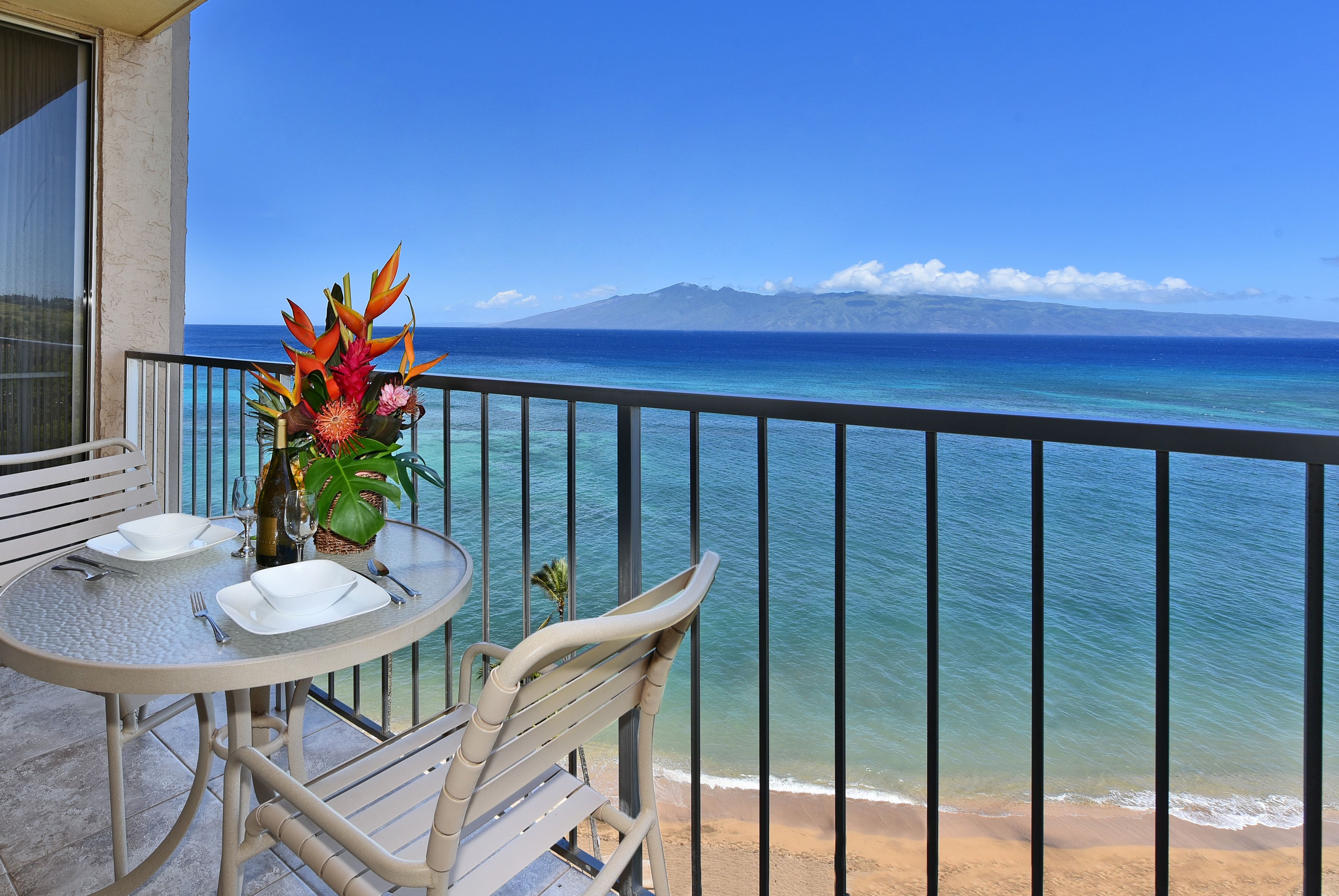 Un balcón con mesa lista para comer, con vista a una playa y al océano.