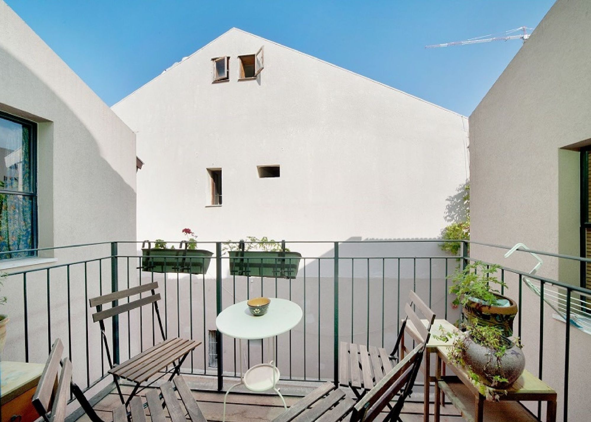A balcony with a table, chairs, and potted plants.