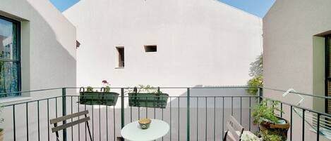 A balcony with a table, chairs, and potted plants.