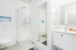 Un bany modern amb dutxa de vidre, vàter blanc i un lavabo amb mirall.