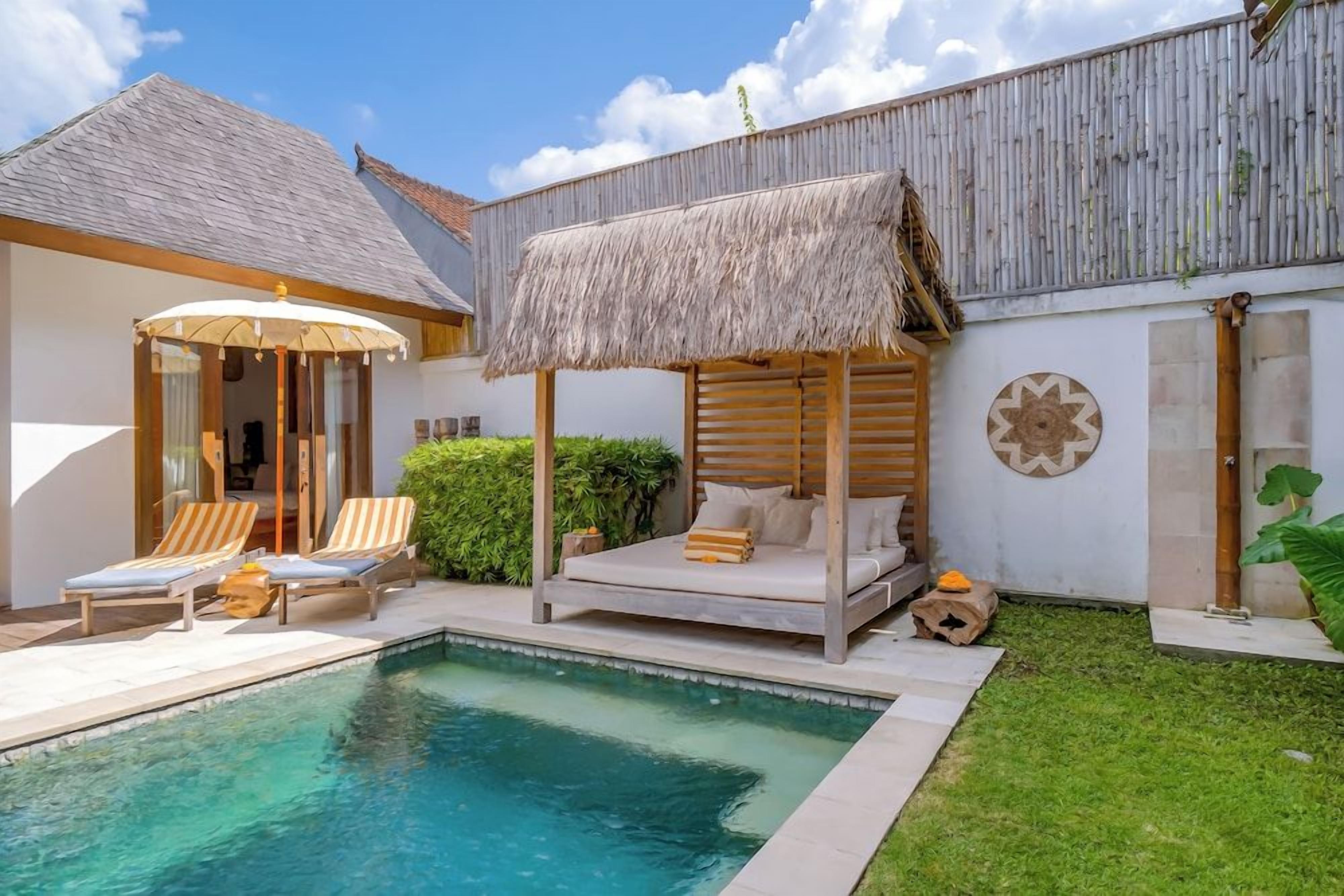 A poolside area with a thatched-roof bed, lounge chairs, and a small pool.