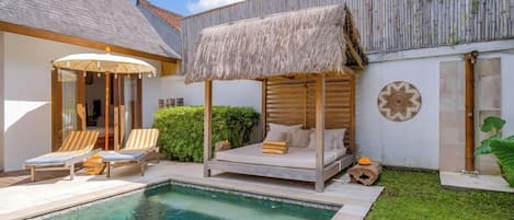 A poolside area with a thatched-roof bed, lounge chairs, and a small pool.