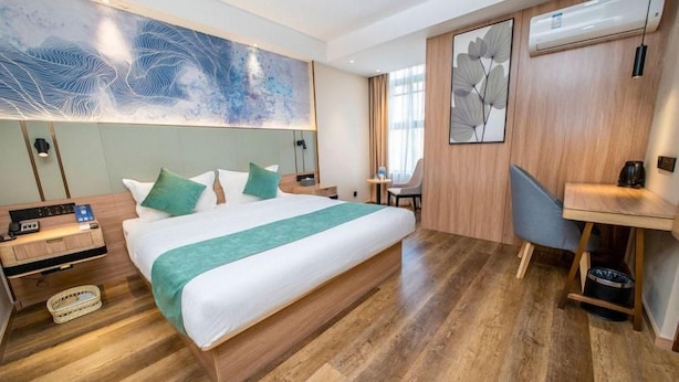 Quarto de hotel com cama grande, escrivaninha, cadeira e ar-condicionado fixado na parede.
