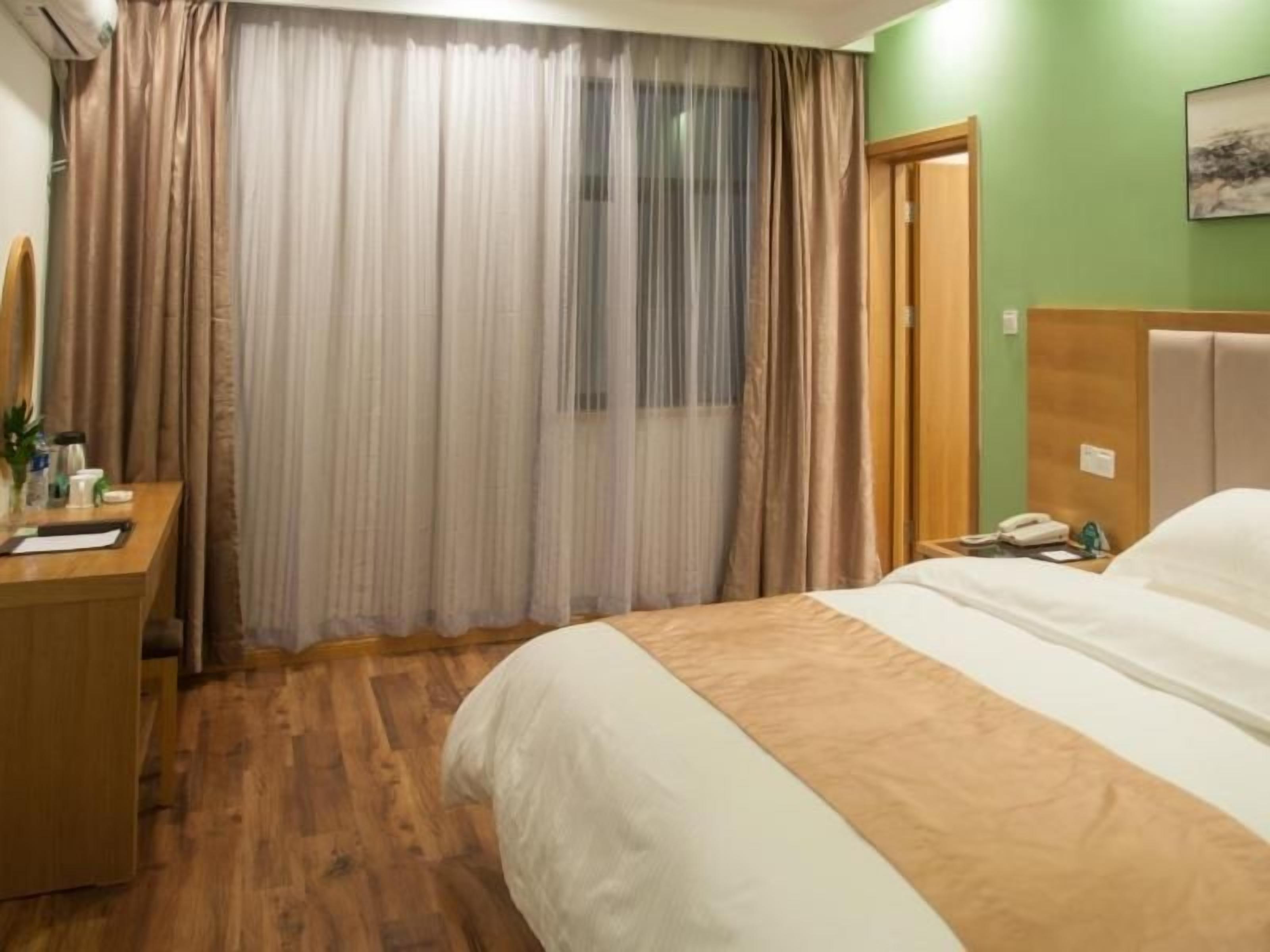 A hotel room with a bed, a wooden desk, a telephone, and a window with curtains.