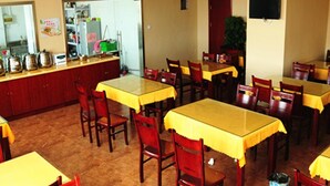Uma sala de jantar com várias mesas e cadeiras, uma cozinha equipada com utensílios e eletrodomésticos, e uma televisão fixada na parede.