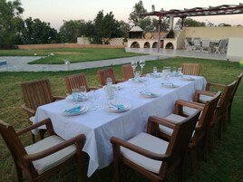 Un área de comedor al aire libre con una mesa dispuesta para seis personas, rodeada de sillas de madera con asientos acolchados.