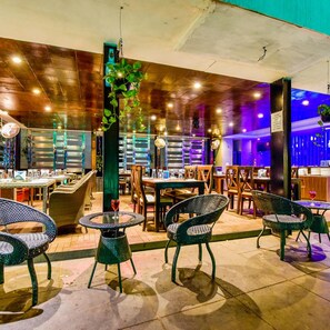 An indoor dining area with round tables and wicker chairs, a vertical garden, and a bar area with stools.