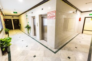 Un hall de hotel con suelo de baldosas, dos ascensores, un cartel que recomienda no usar los ascensores en caso de incendio y una señal de salida verde.