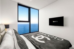 A bedroom with a large window, a bed with a Chanel blanket, a TV on the wall, and a lamp on the nightstand. - The Mojo Ocean Suite Sixty-Sixth Floor, Meriton (Surfers Paradise)