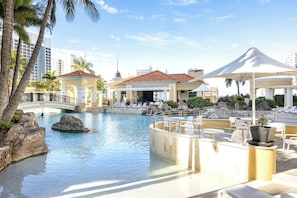 Poolbereich eines Resorts mit einer Brücke, Liegestühlen und Blick auf die Skyline der Stadt.