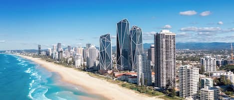 A coastal cityscape with high-rise buildings, a sandy beach, and a clear blue sky.