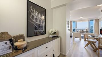 A hotel room with a large window, a dining area with a table and chairs, and a wall-mounted artwork.