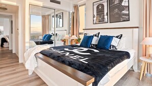 Un dormitorio de hotel con una cama grande, vistas a través de un ventanal y un cartel de Givenchy en la pared.