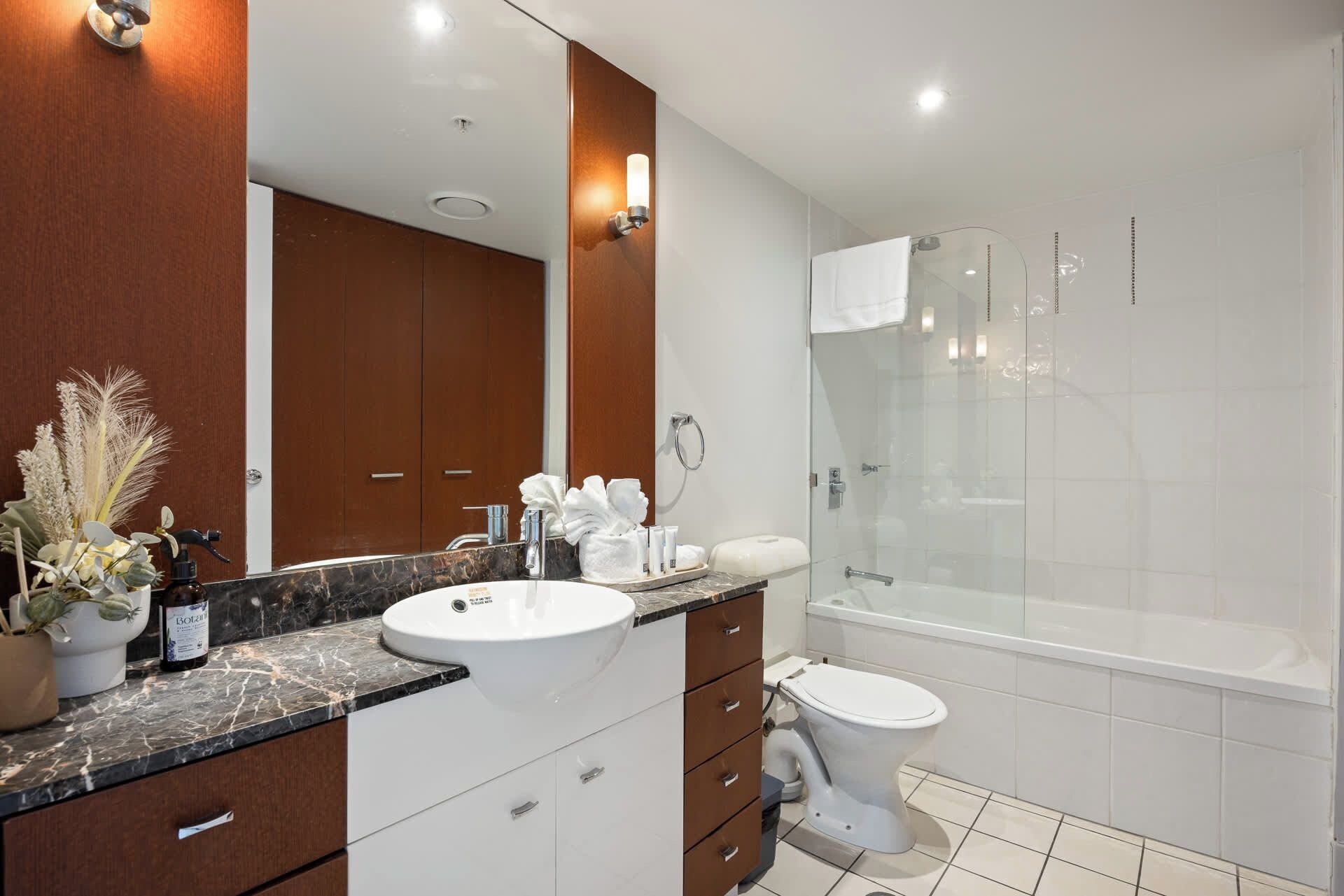 Une salle de bain moderne avec un comptoir en marbre, un lavabo blanc, une douche à parois de verre et des toilettes.