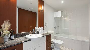 Une salle de bain moderne avec un comptoir en marbre, un lavabo blanc, une douche à parois de verre et des toilettes.