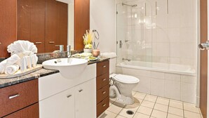 Un baño moderno con lavamanos, espejo, inodoro y ducha con mampara de vidrio.