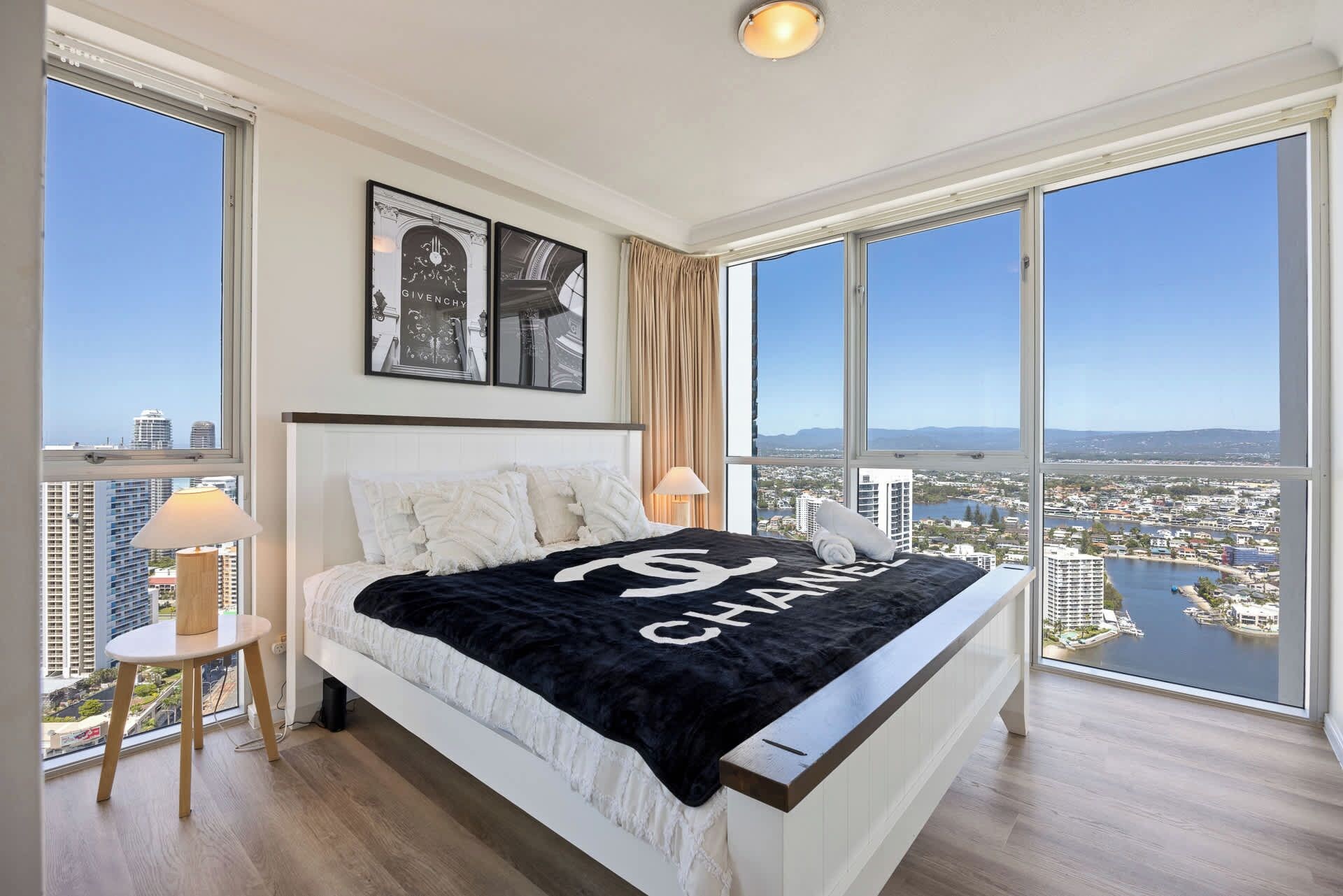 Ein Schlafzimmer in einem Hochhaus mit einem großen Bett, zwei Nachttischlampen und Blick auf Stadt und Wasser.