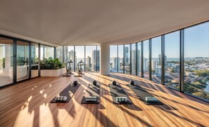 Amplia habitación con ventanas grandes, equipo de ejercicio y vista a un paisaje urbano.