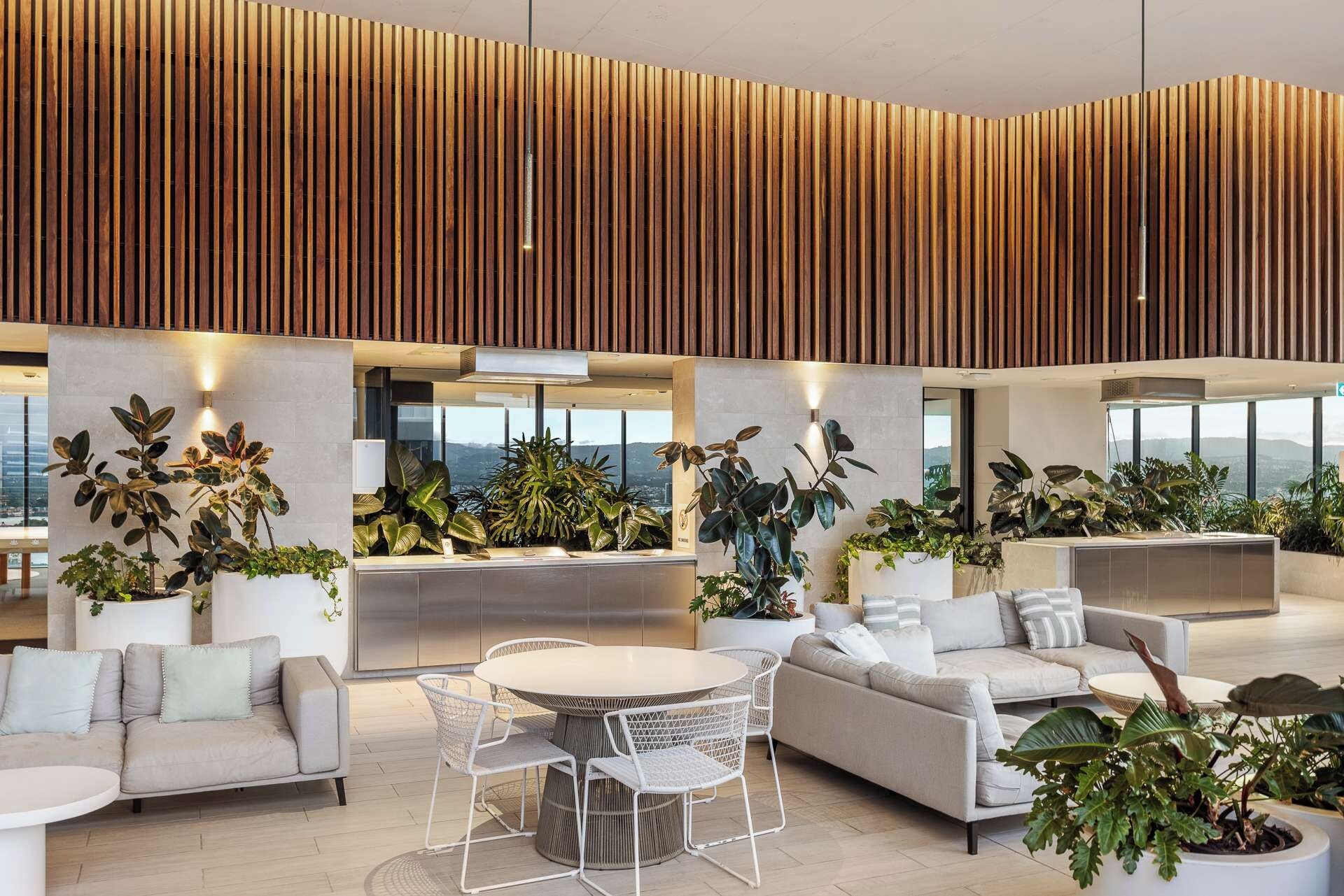 Un espacio interior moderno con techo alto, listones de madera verticales y una zona de estar central con una mesa redonda y sillas.