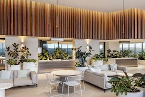 Un espacio interior moderno con techo alto, listones de madera verticales y una zona de estar central con una mesa redonda y sillas.