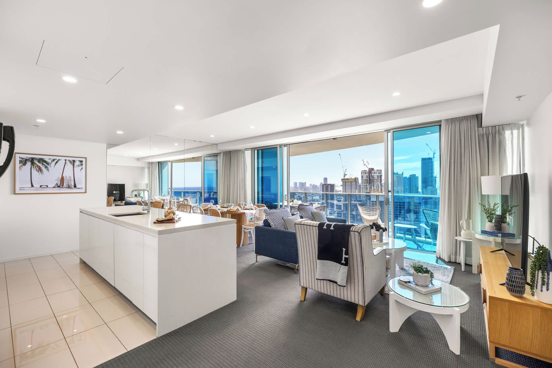 Una habitación de hotel moderna con un balcón grande, un área de comedor y vistas del horizonte de la ciudad.
