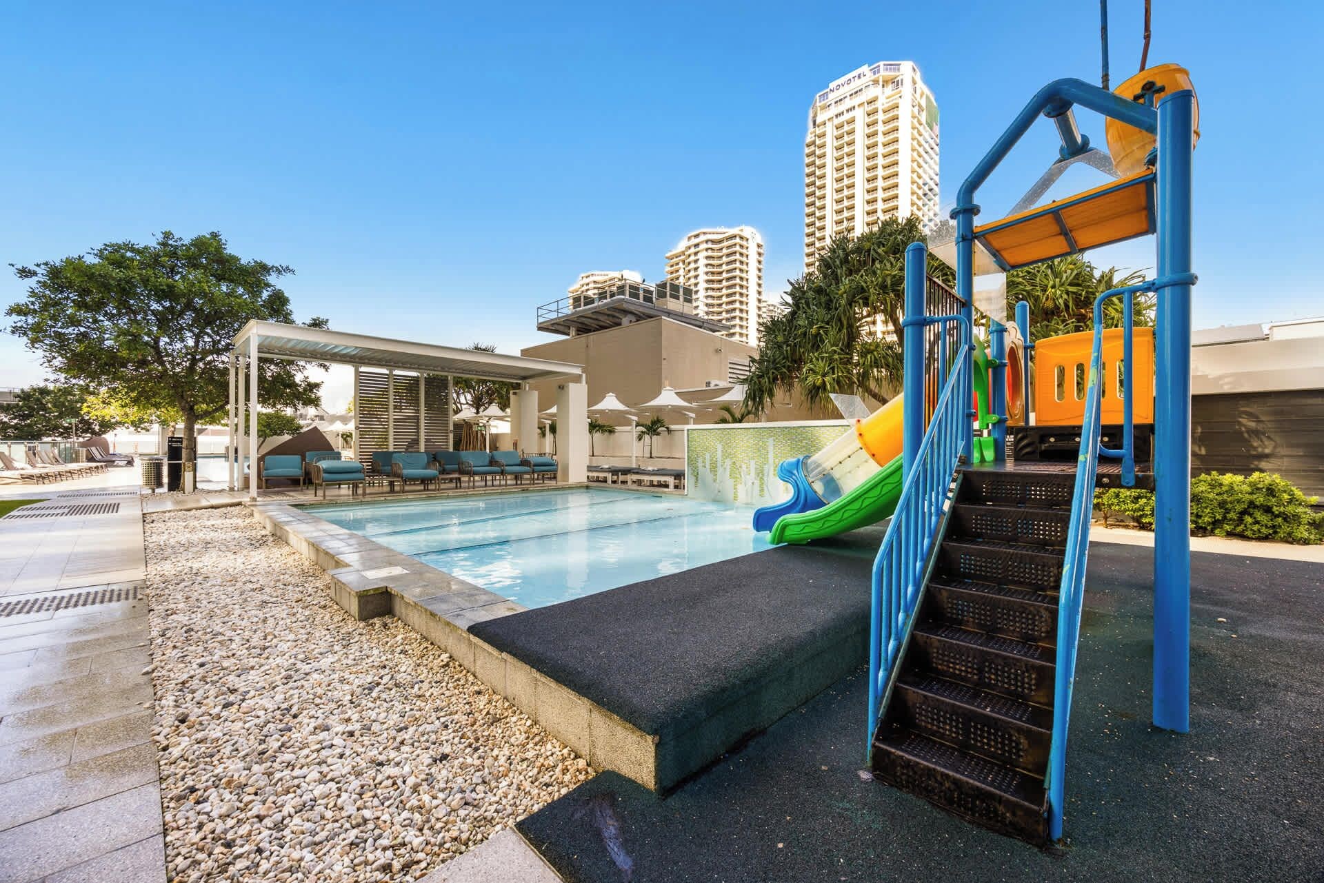 A swimming pool with a slide, lounge chairs, and a covered seating area.