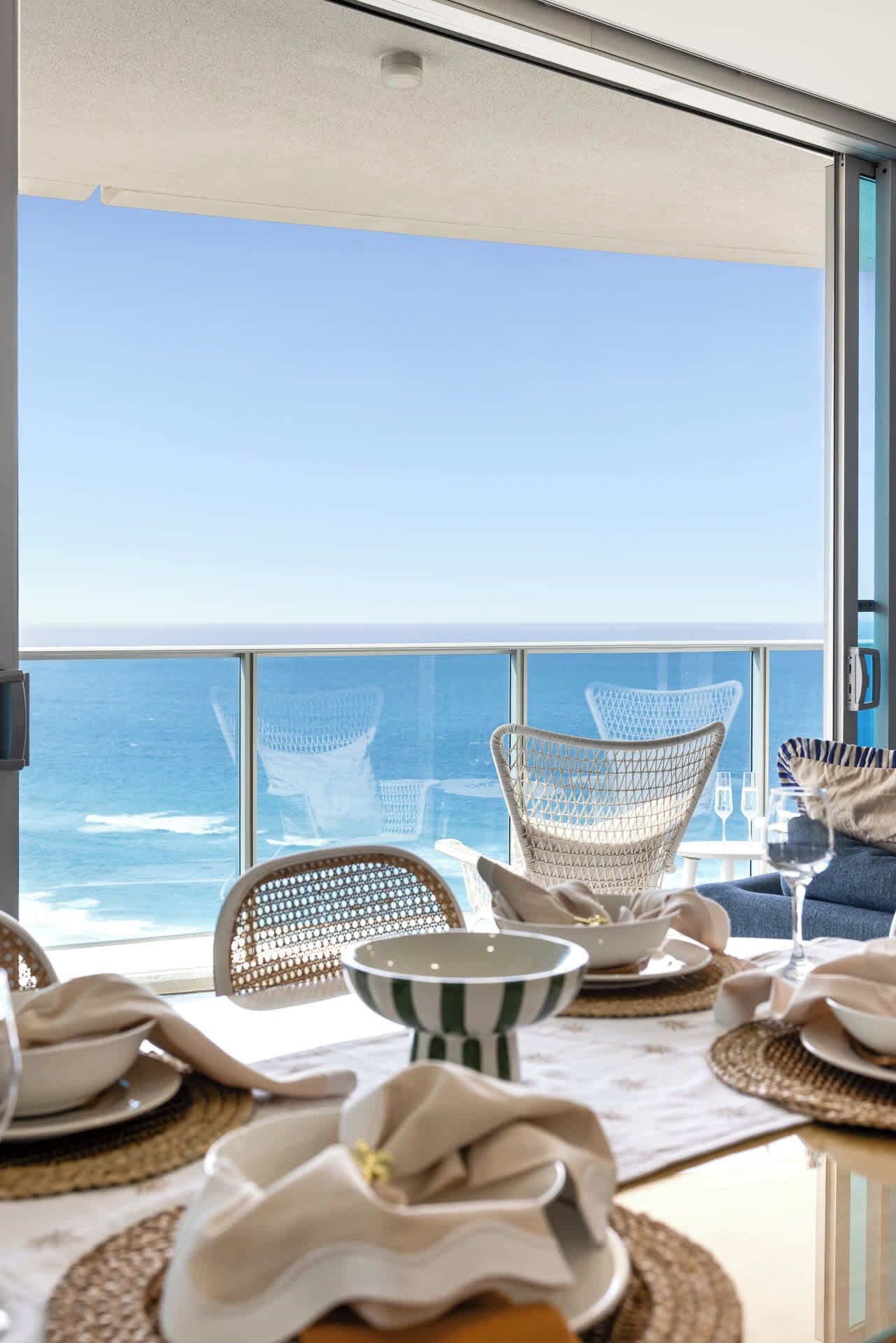 Comedor con vistas al océano, con sillas de mimbre y una mesa preparada para dos.