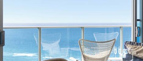A dining area with a view of the ocean, featuring wicker chairs and a table set for two.