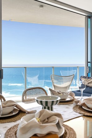 A dining area with a view of the ocean, featuring wicker chairs and a table set for two. - Hilton Surfers | Vogue on Orchid | 2BR Ocean View (Surfers Paradise)