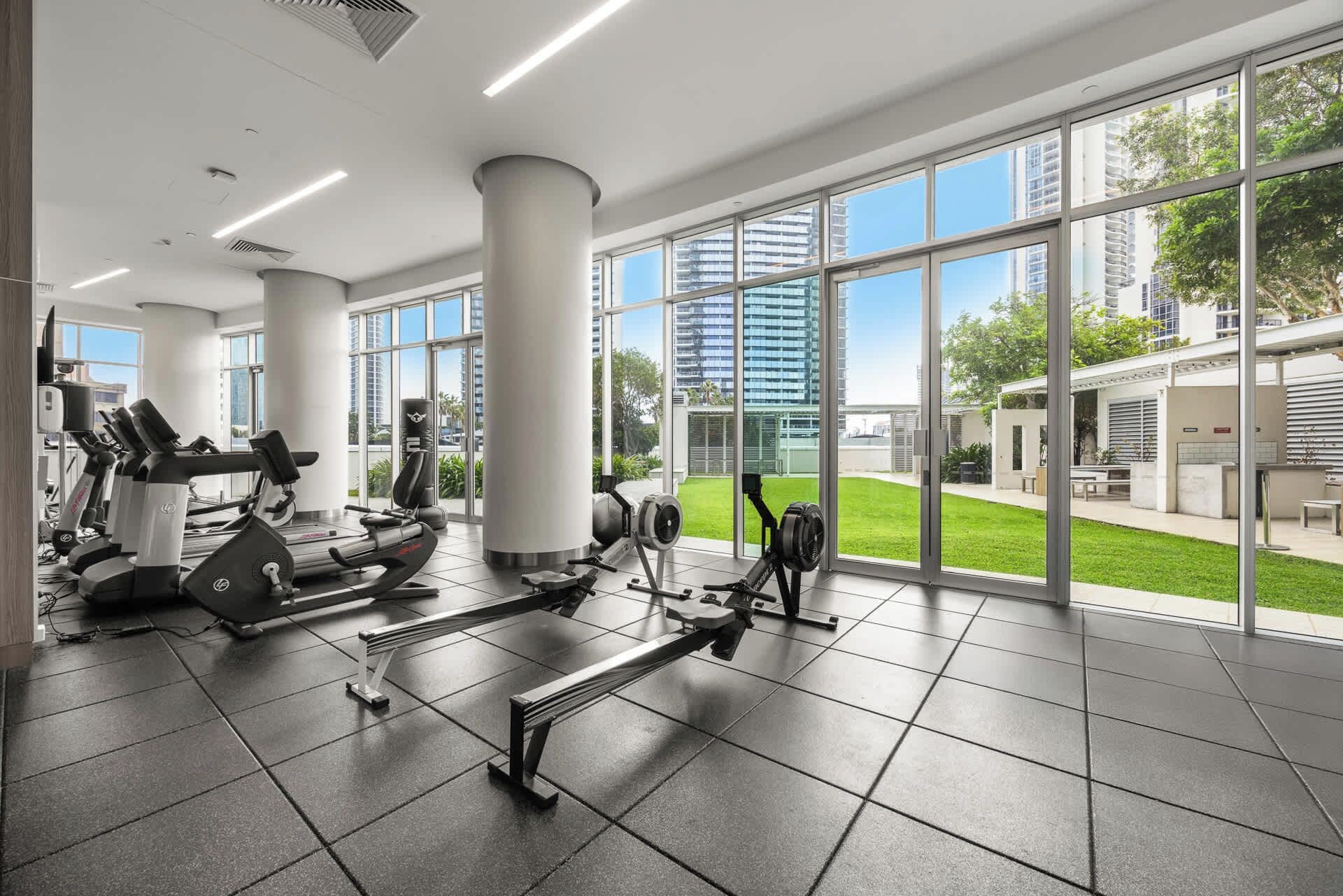 A gym with exercise equipment, large windows, and a view of buildings and greenery.