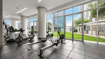 A gym with exercise equipment, large windows, and a view of buildings and greenery.