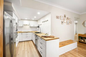 A modern kitchen with white cabinetry, a wooden countertop, and a built-in bench. - The Golden Hour Chevron Renaissance 2BR, Surfers (Surfers Paradise)