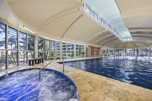 A large indoor swimming pool with a jacuzzi area, glass windows, and a high ceiling. - The Golden Hour Chevron Renaissance 2BR, Surfers (Surfers Paradise)