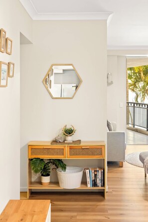 A living room with a wooden console table, a mirror, and a view of the outdoors. - The Golden Hour Chevron Renaissance 2BR, Surfers (Surfers Paradise)