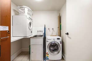 A compact laundry room with a front-loading washer, a stacked washer, and a small sink. - The Golden Hour Chevron Renaissance 2BR, Surfers (Surfers Paradise)