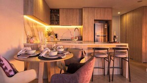 A modern kitchen with a central island, bar stools, and a dining area with a round table and chairs. - Broadbeach 2BR | Atelier 35, Casino Towers (Broadbeach)