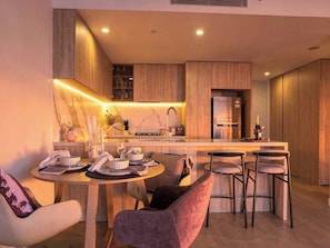 A modern kitchen with a central island, bar stools, and a dining area with a round table and chairs. - Broadbeach 2BR | Atelier 35, Casino Towers (Broadbeach)