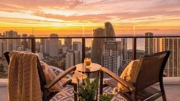 A balcony with a city view at sunset, featuring a table with a candle, two chairs, and a potted plant. - Broadbeach 2BR | Atelier 35, Casino Towers (Broadbeach)