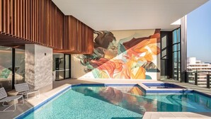 A rooftop swimming pool with a mural, lounge chairs, and a view of the city. - Broadbeach 2BR | Atelier 35, Casino Towers (Broadbeach)