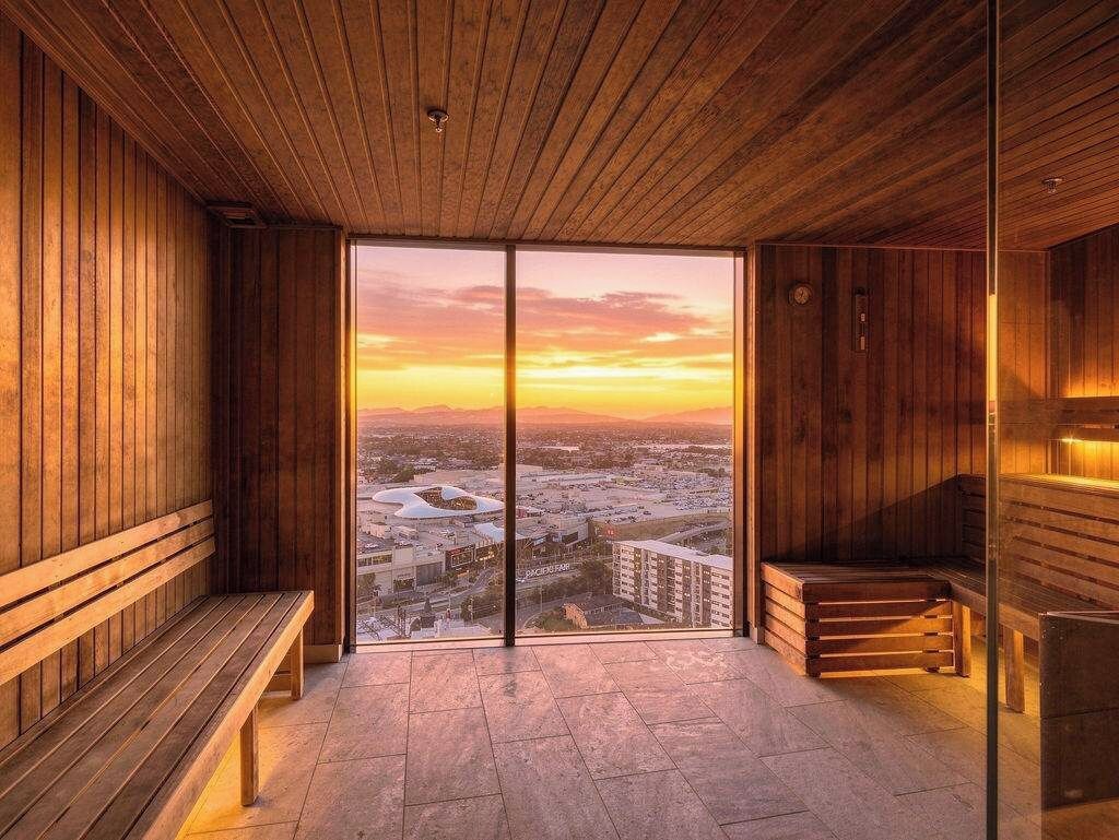 Ein Saunaraum mit Holzbänken und einer großen Glastür, die zu einem Außenbereich führt.