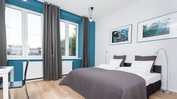 A modern bedroom with a large bed, a desk, and a view of the city through the window. - Krakow B And B (Kraków)