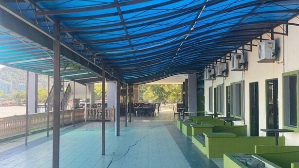 Uma área externa coberta com piso de azulejos, assentos verdes e aparelhos de ar condicionado.