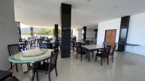 Uma ampla área de refeições interna com várias mesas e cadeiras, pilares imponentes e vista para o exterior.