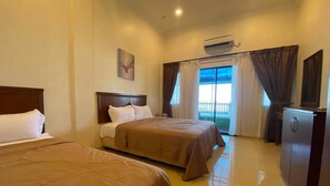 Quarto de hotel com duas camas, um refrigerador e uma janela com cortinas.