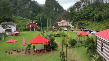 A rural setting with a red-roofed pavilion, a white building, and a parking area with cars.