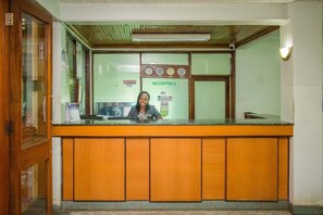 A reception desk with a wooden counter, a glass partition, and a wall-mounted clock. - Desmond Tutu Guest House (Nairobi)