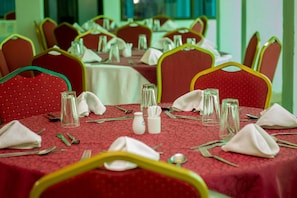 A dining area with tables set for multiple guests, featuring red upholstered chairs with green trim, white tablecloths, and neatly arranged cutlery and glassware. - Desmond Tutu Guest House (Nairobi)